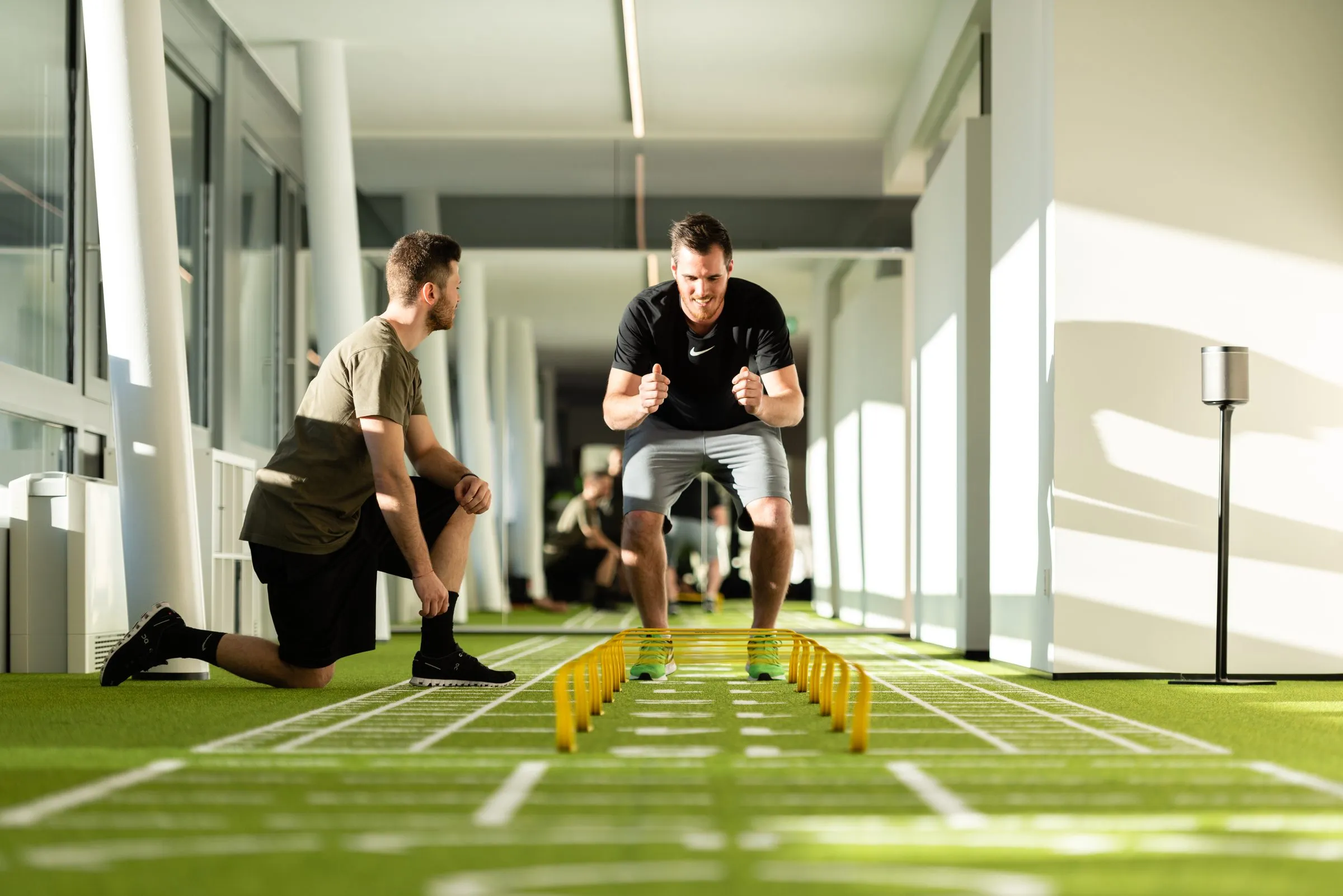 Athlete jumping over mini hurdles on the artificial turf track, with a trainer kneeling next to them
