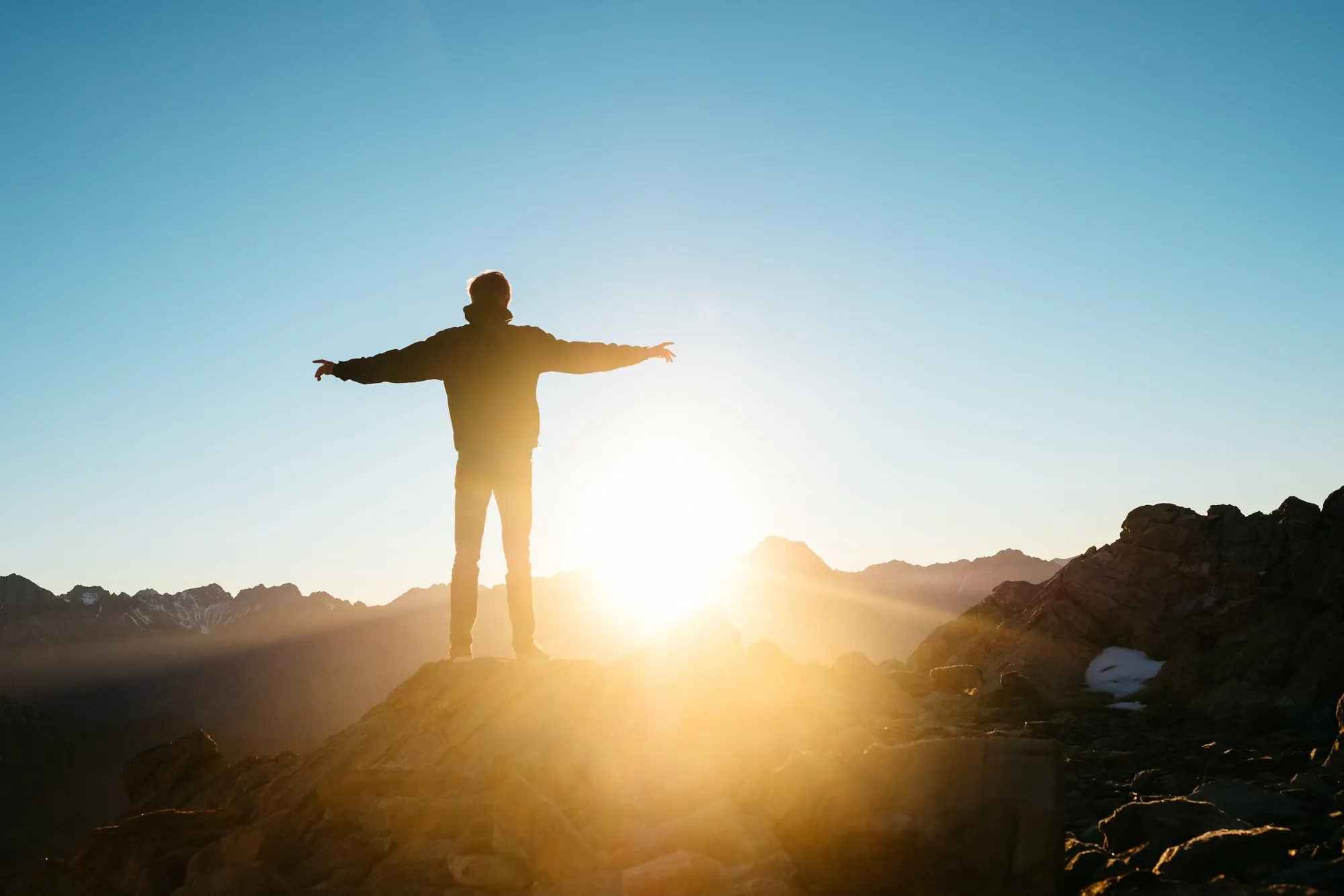 Person with outstretched arms on a mountain summit at sunrise