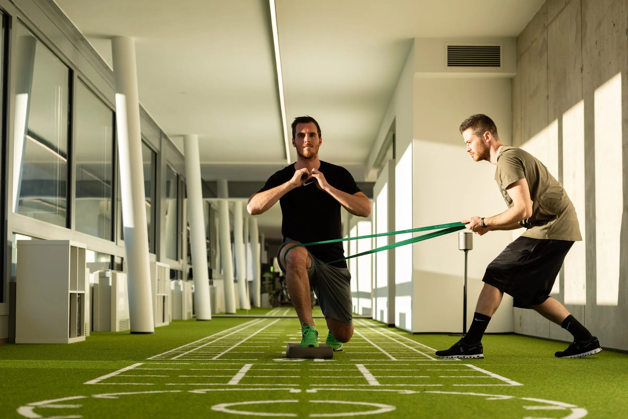 Athlete training with a resistance band while a trainer holds the band on the artificial turf track